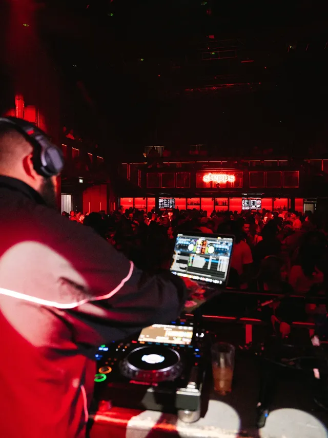The view from behind the decks towards a red-lit crowd.